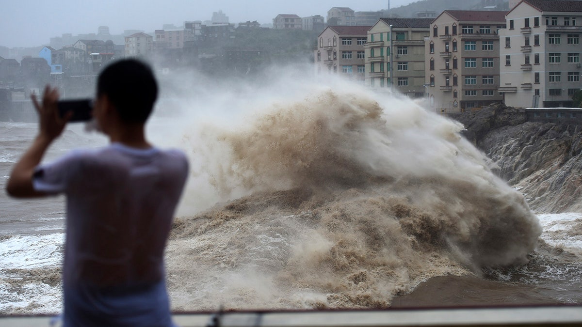 In this Aug. 9, 2019, photo released by Xinhua News Agency, a man uses his mobile phone to record waves crashing on the shore as typhoon Lekima approaches the Shitang Township of Wenling City in eastern China's Zhejiang Province. Typhoon Lekima stuck the coast south of Shanghai, knocking down houses and trees.