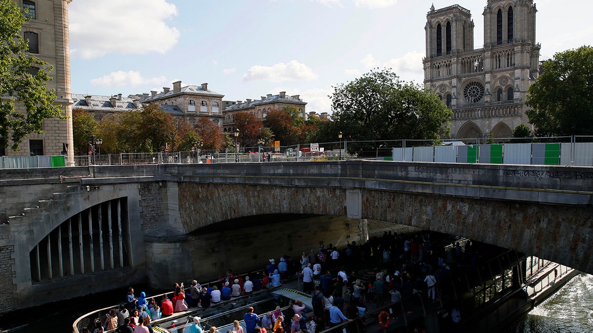 Tourists in a boat pass under a bridge near the Notre Dame cathedral in Paris, Tuesday, Aug. 13, 2019. Workers are preparing to decontaminate some Paris streets surrounding the Notre Dame Cathedral that have been tested with high levels of lead following the April blaze that damaged the landmark. 