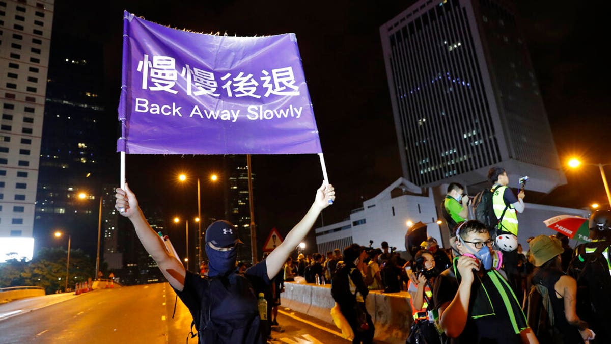 A demonstrator holding up a sign reading "Back away slowly" to encourage other demonstrators to leave, near the Chinese Liaison Office in Hong Kong on Sunday. (AP Photo/Vincent Thian)