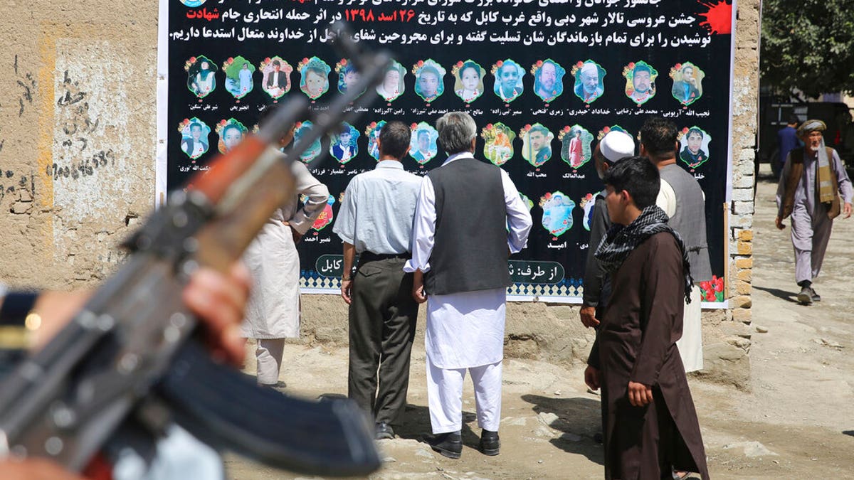 Afghans look at a banner displaying photographs of victims of the Dubai City wedding hall bombing during a memorial service, in Kabul, Afghanistan, Tuesday, Aug. 20, 2019.