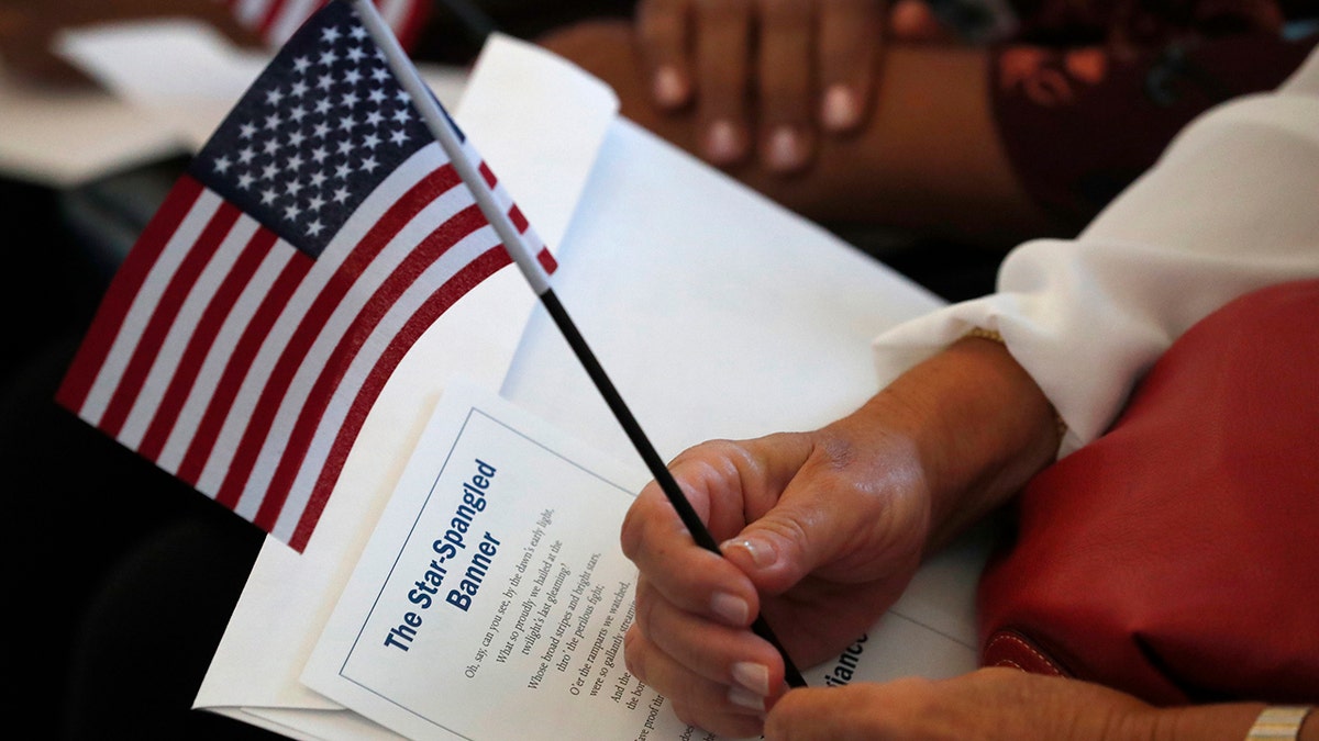 FILE - In this Aug. 16, 2019, file photo a citizen candidate holds an American flag and the words to The Star-Spangled Banner before the start of a naturalization ceremony at the U.S. Citizenship and Immigration Services Miami field office in Miami. (AP Photo/Wilfredo Lee)