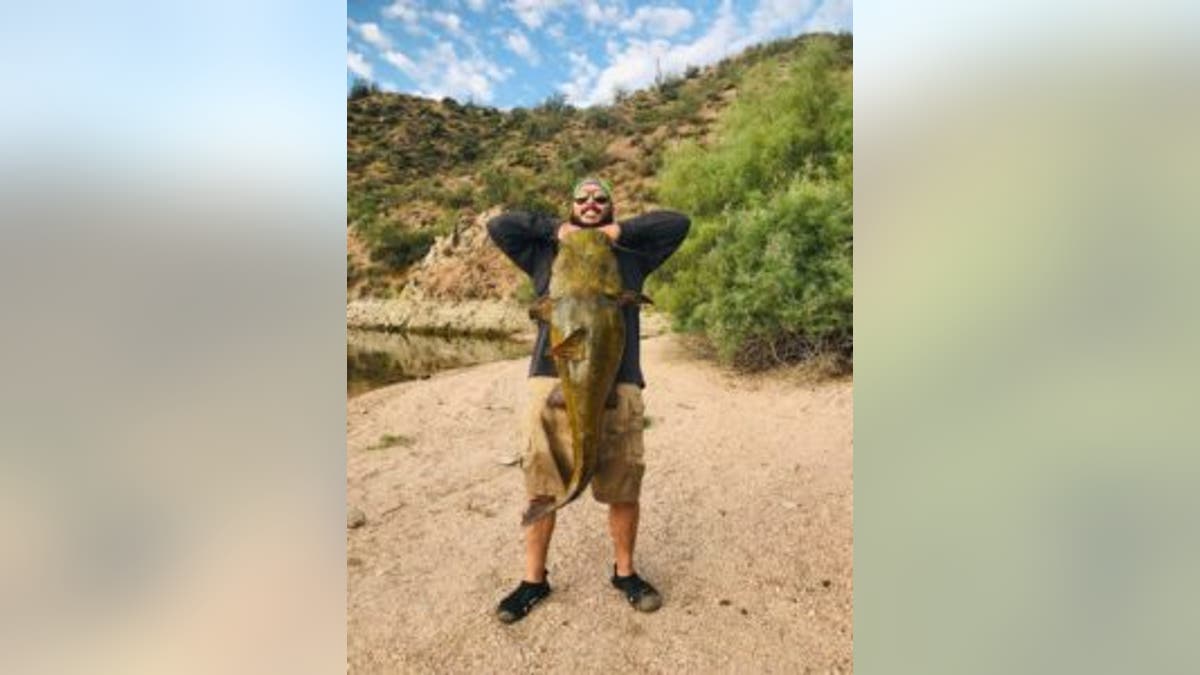 Erick Barrantes holding up a massive catfish that he has caught. 