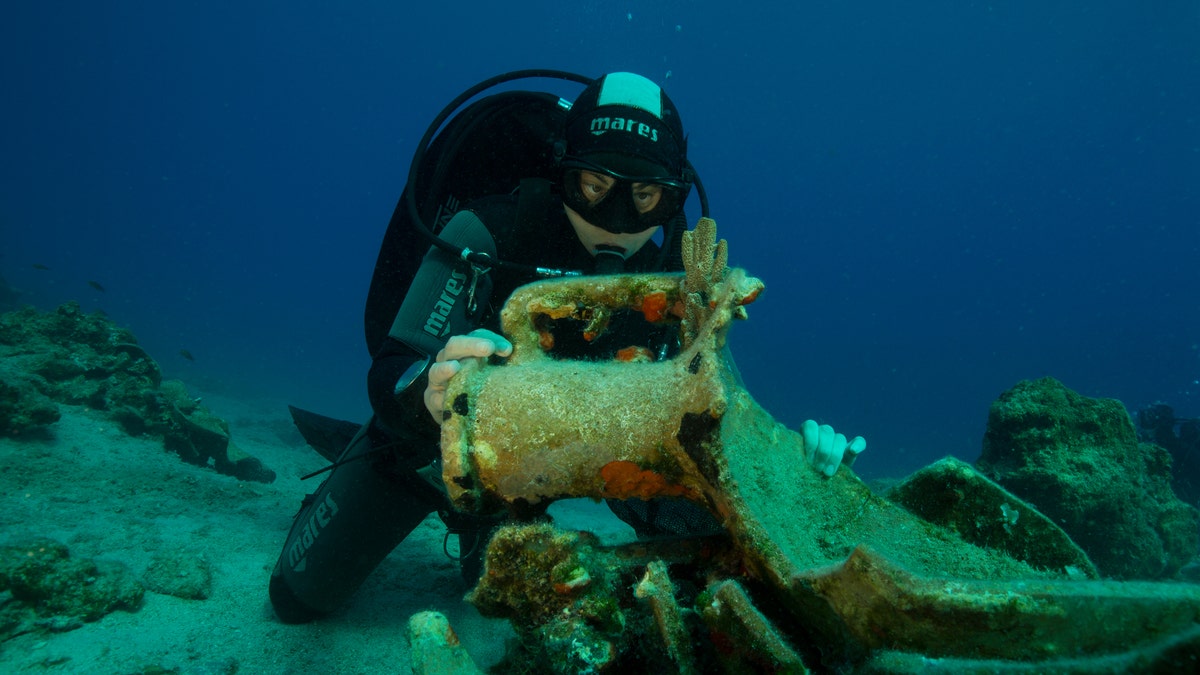 A diver inspects an amphora, or ancient jar, on the seabed.