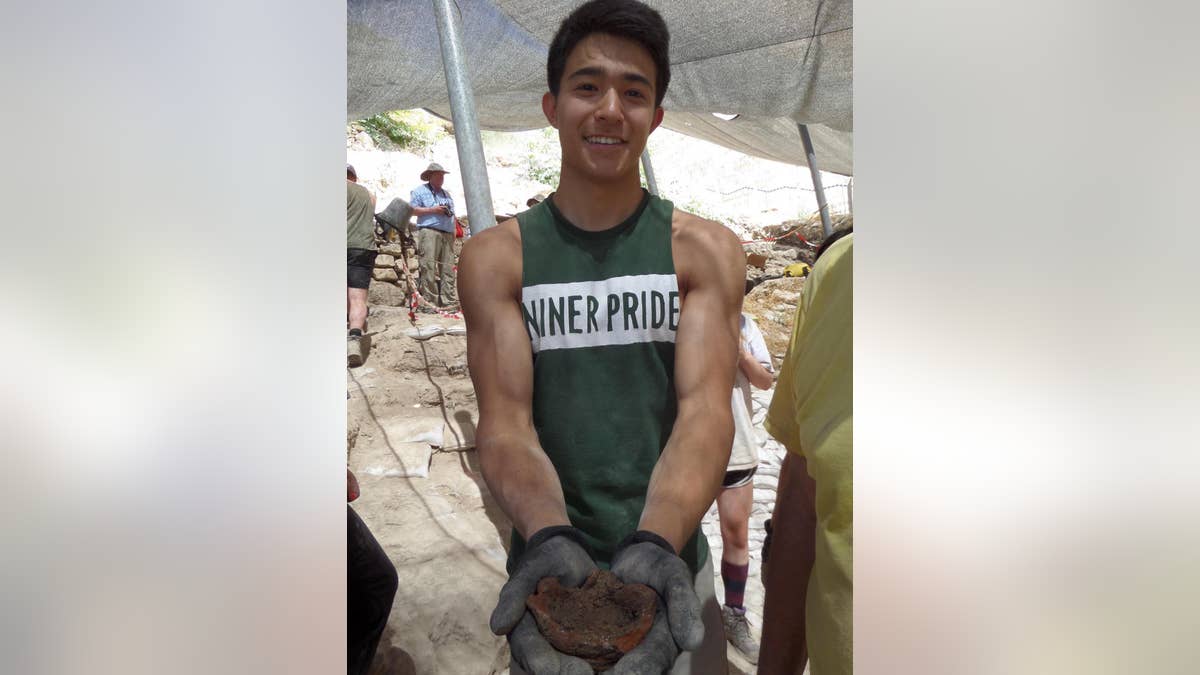 UNC Charlotte student Miles Shen holding a lamp dating from the Iron Age.