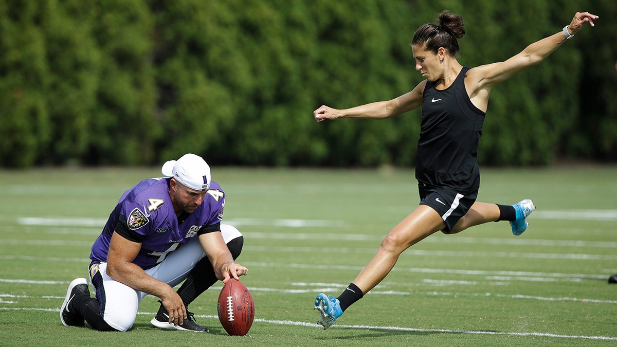 Baltimore Ravens' Sam Koch holds the ball for United States soccer player Carli Lloyd as she attempts to kick a field goal after the Philadelphia Eagles and the Baltimore Ravens held a joint NFL football practice in Philadelphia, Tuesday, Aug. 20, 2019. 