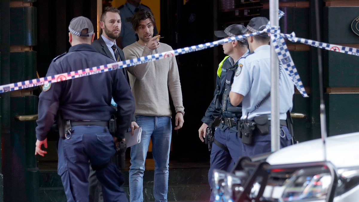 A man, center, points as he assists police at a building where a person has been found dead after a man attempted to stab multiple people in Sydney, Australia, Tuesday, Aug. 13, 2019.
