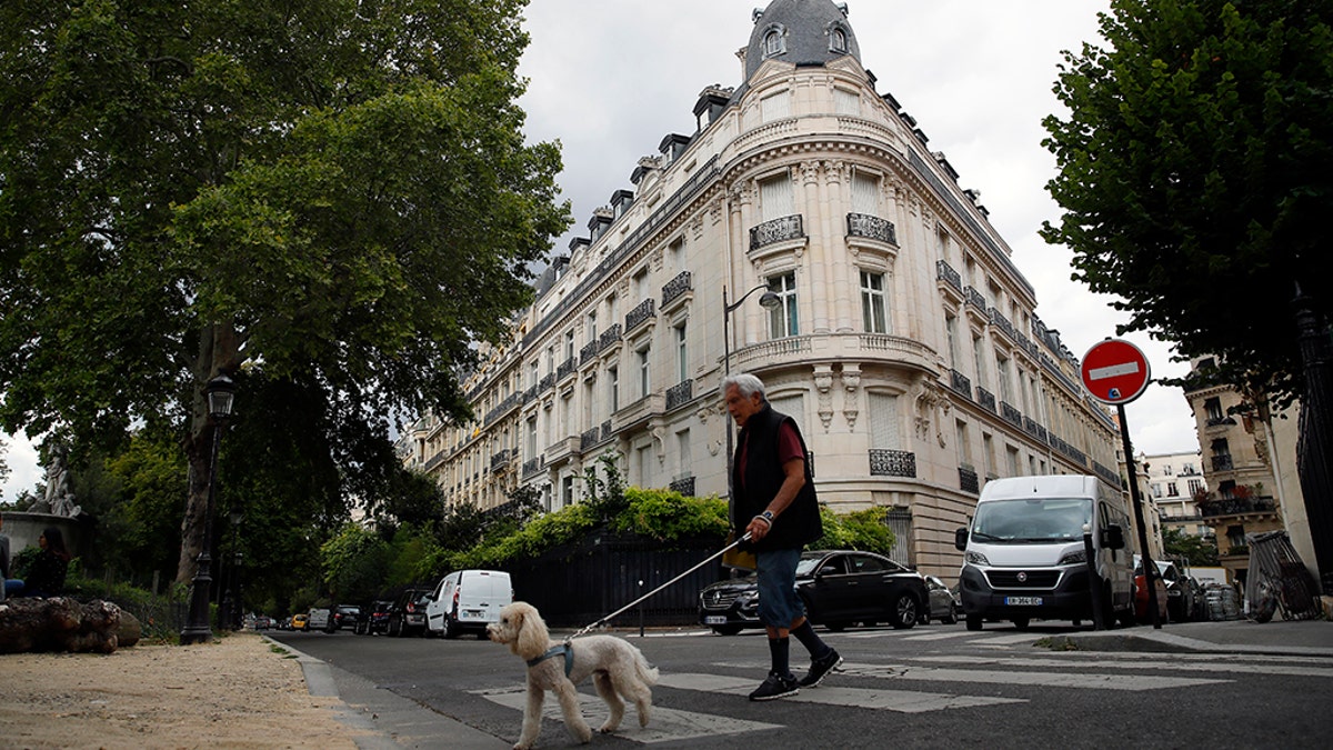 A man walks his dog next to an apartment building owned by Jeffrey Epstein in the 16th district in Paris, Tuesday, Aug. 13, 2019. France's government wants prosecutors to open an investigation into Jeffrey Epstein's links to France following his death in a Manhattan jail cell. U.S. authorities say Epstein had a residence in Paris and used a fake Austrian passport to travel to France in the 1980s.