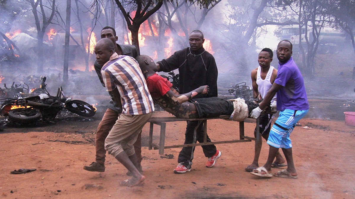 An injured man is carried from the scene as a petrol tanker burns in the background. (AP Photo)