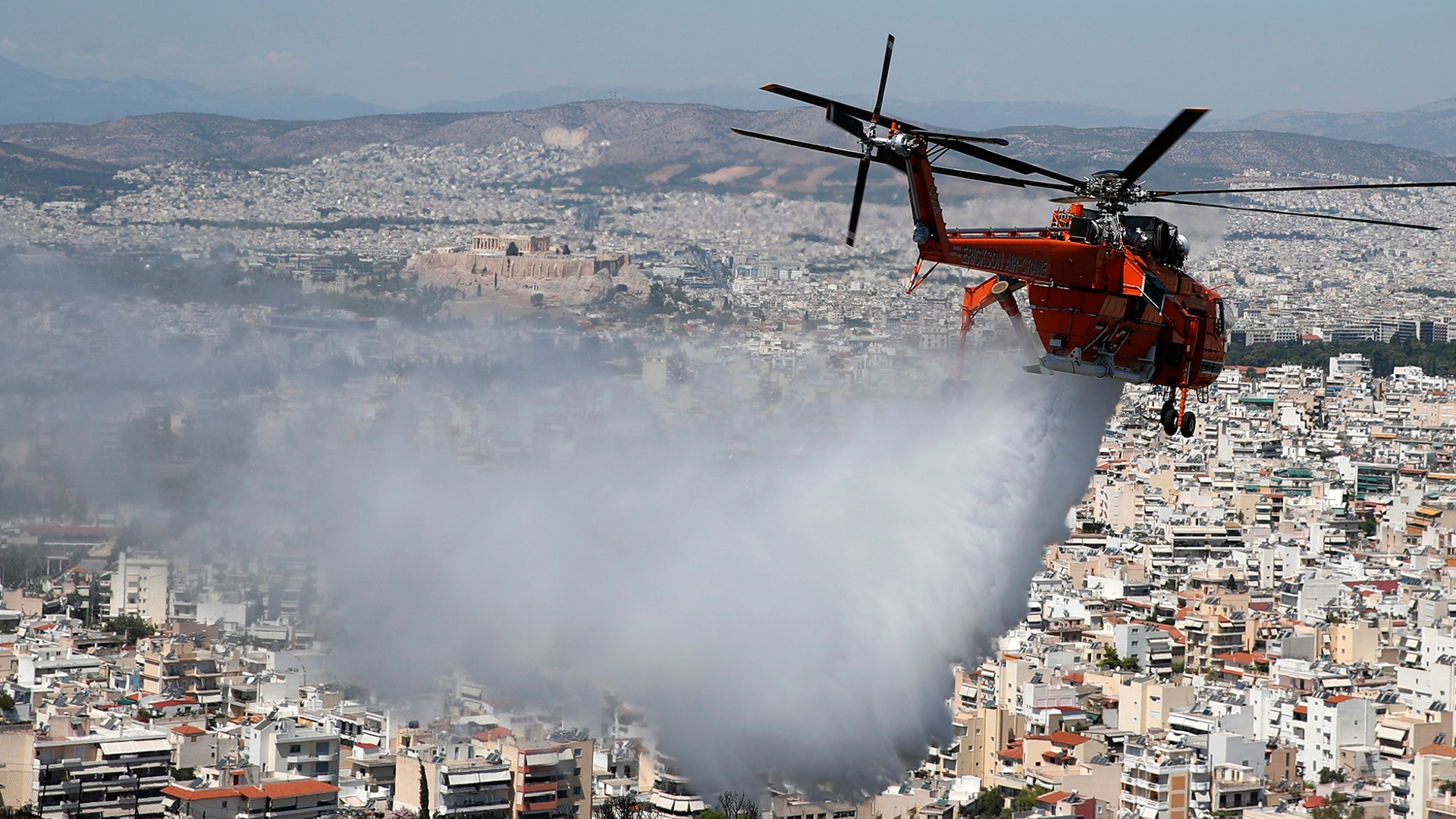 A helicopter drops water over a hill stopping a wildfire in the eastern Athens suburb of Vironas as the ancient Acropolis hill is seen in the background, Aug. 28, 2019. 