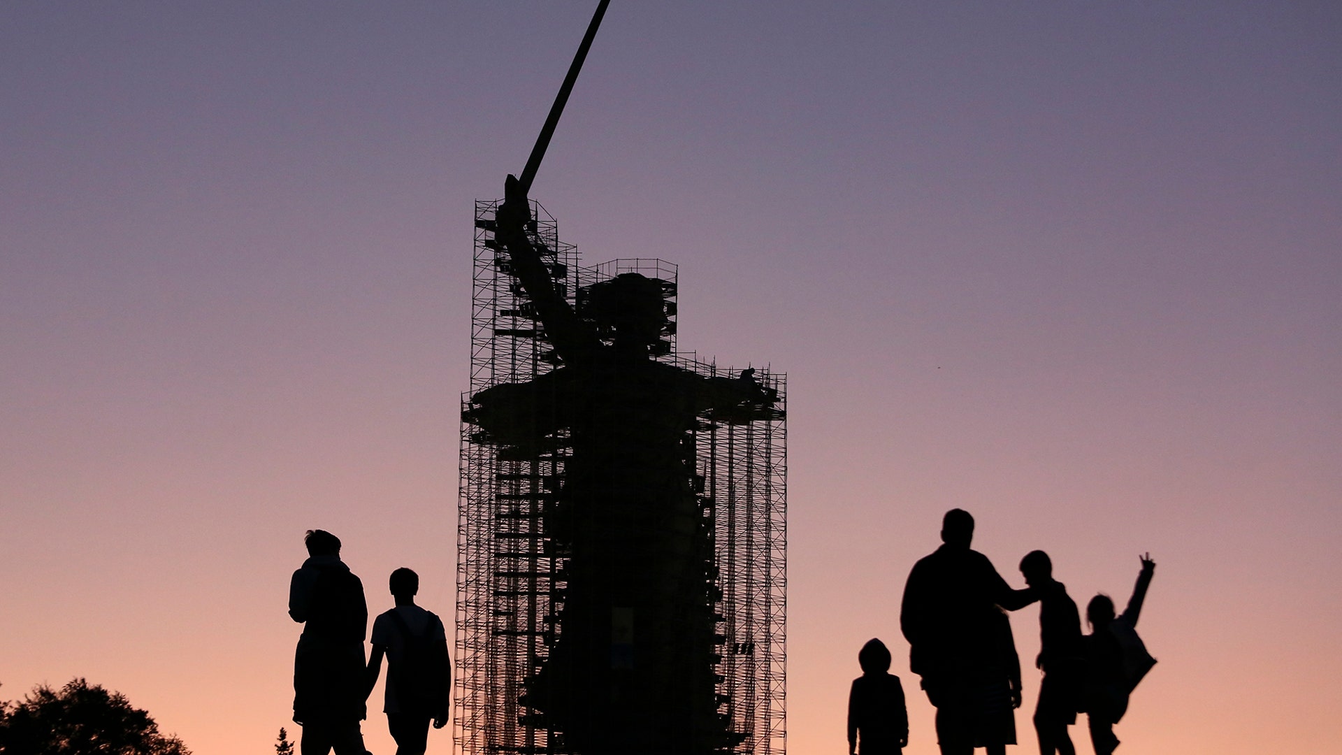 People walk near the statue 'The Motherland Calls' under reconstruction in Mamayev Kurgan, the main place of the Battle of Stalingrad memorial, during sunset in Volgograd, Russia, Aug. 12, 2019.