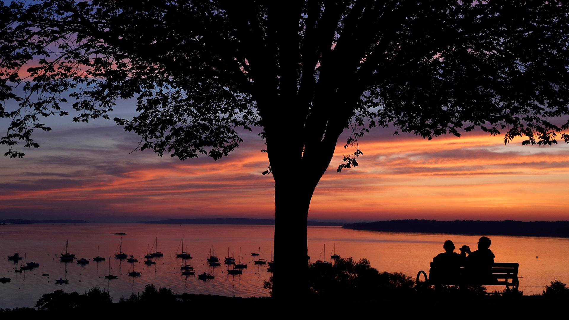 An early-rising couple is rewarded with a colorful sunrise over Casco Bay, in Portland, Maine, Aug. 21, 2019. 
