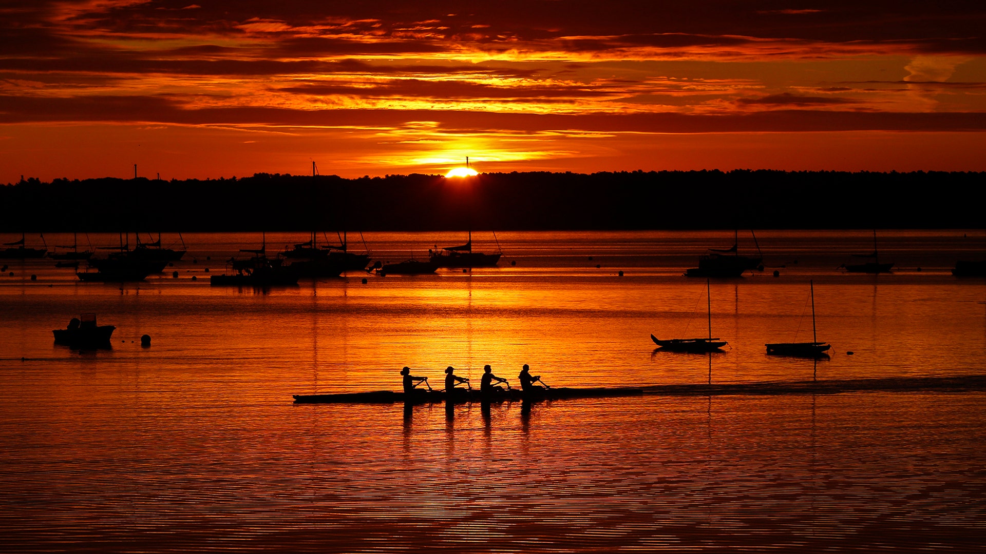 A quad scull of rowers begins their workout on Casco Bay as the sun starts to peak over Great Diamond Island, in Portland, Maine, Aug. 28, 2019. 