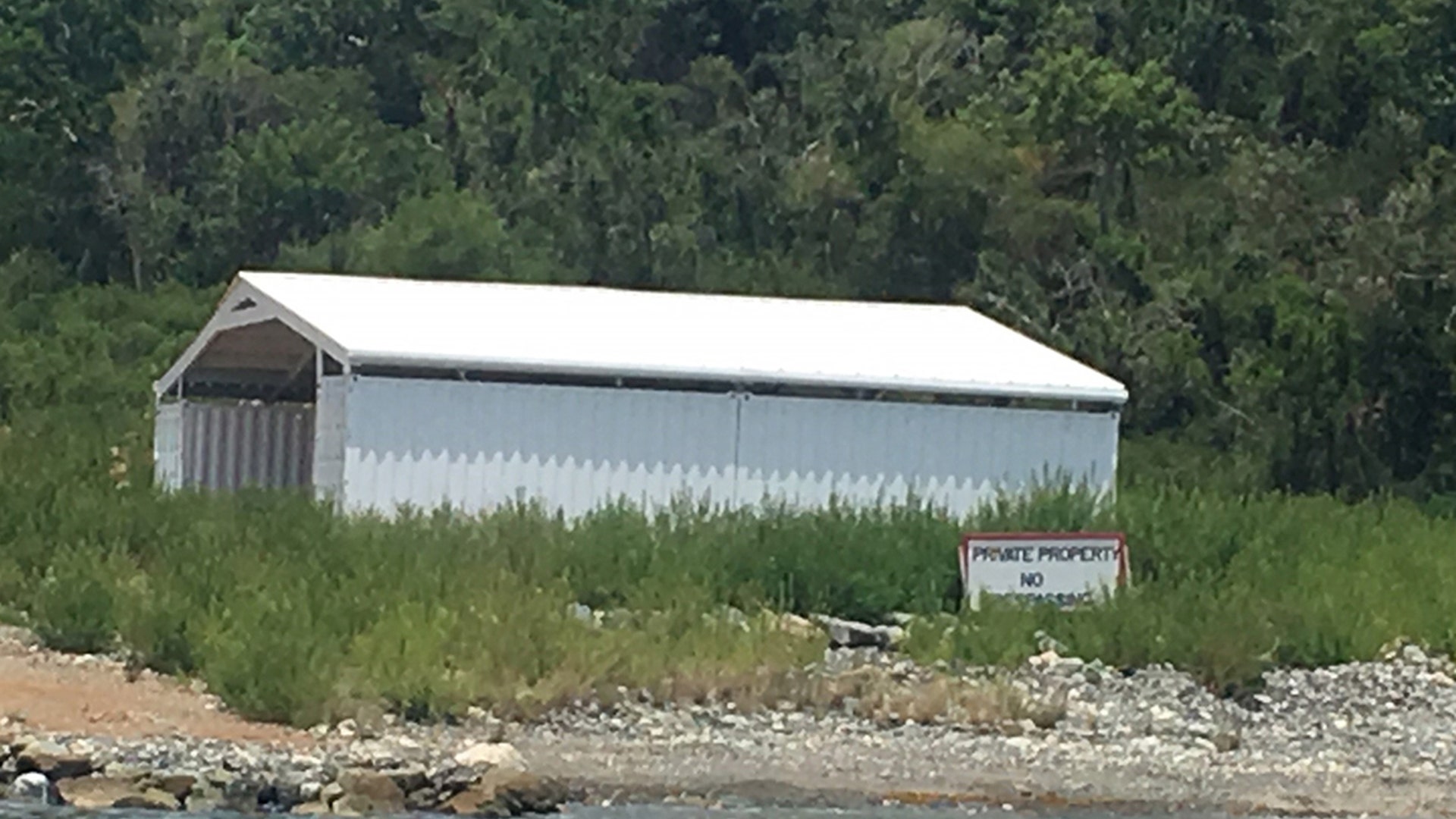 A white structure next to a red and write "private property" sign located just above the shorline on Little St. James Island. The island was purchased by Epstein 21 years ago. 