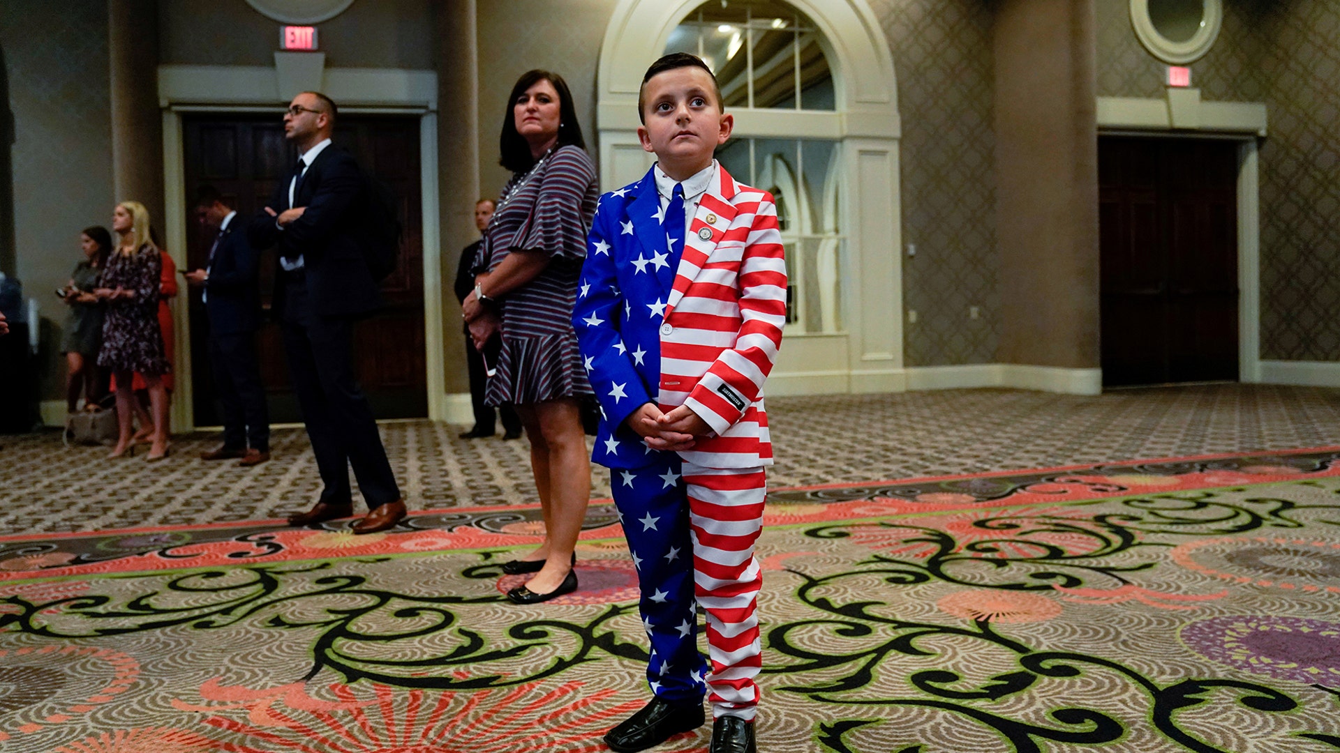 9-year-old Reed Elliotte stands in the back of the room in a U.S. flag outfit with his mother Larrietta listening to U.S. President Donald Trump address the AMVETS American Veterans convention in Louisville, Aug. 21, 2019. 