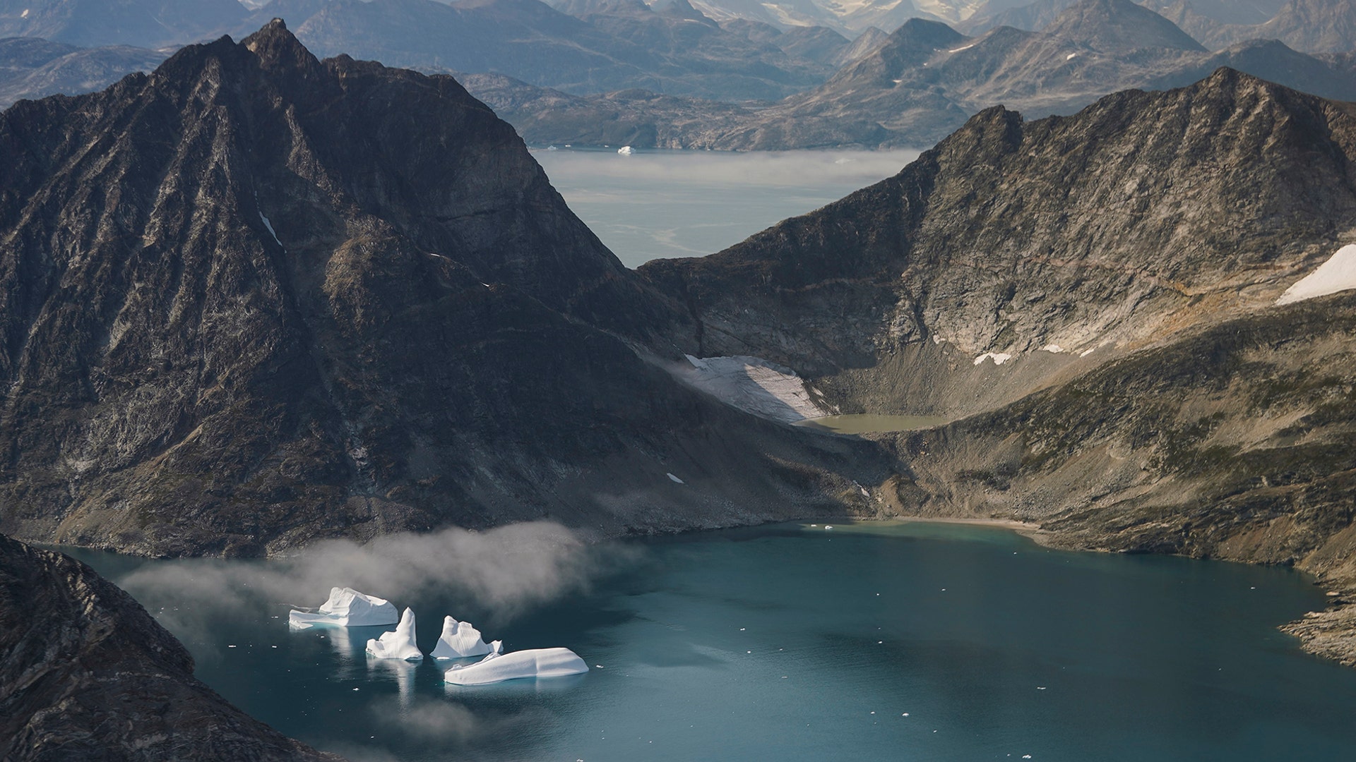 Icebergs are photographed from the window of an airplane carrying NASA Scientists as they fly on a mission to track melting ice in eastern Greenland, Aug. 14, 2019