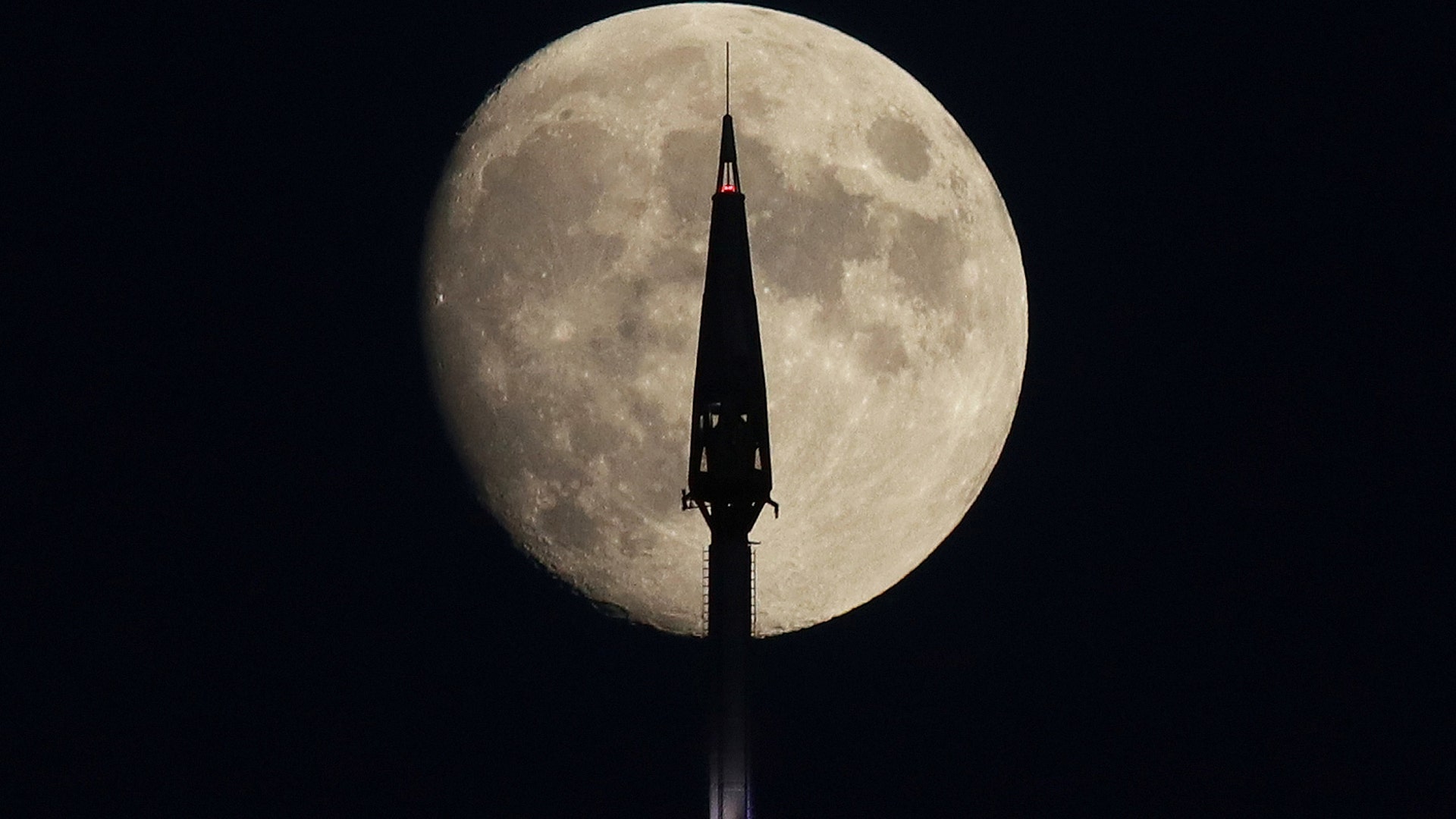 The moon rises behind the spire of One World Trade Center in New York City, Aug. 13, 2019.