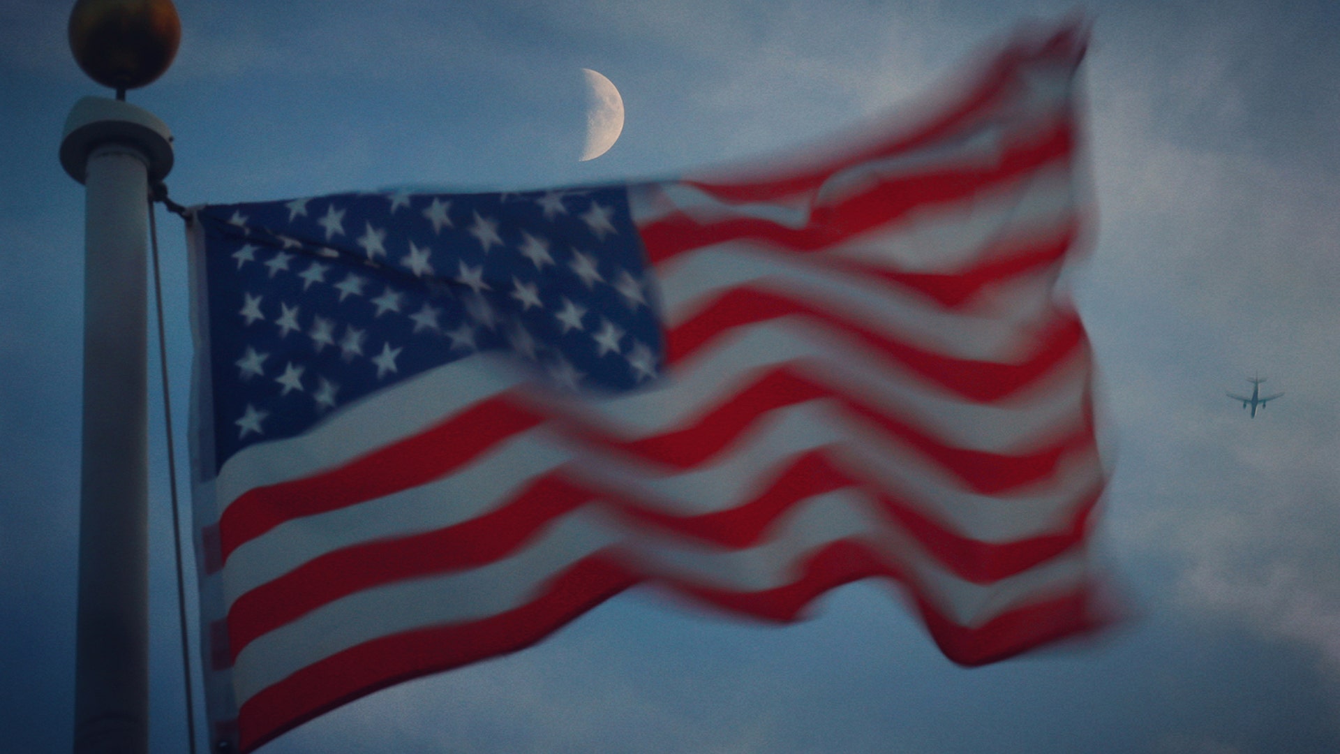 The moon rises over a flag at sunset in Jersey City, New Jersey, Aug. 6, 2019.