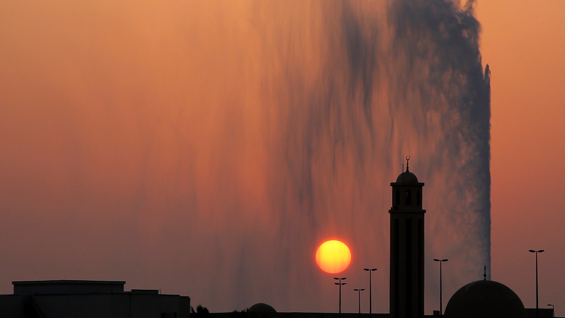 The setting sun drops behind a mosque and the landmark Jiddah fountain, in Jiddah, Saudi Arabia, Aug. 29, 2019. 