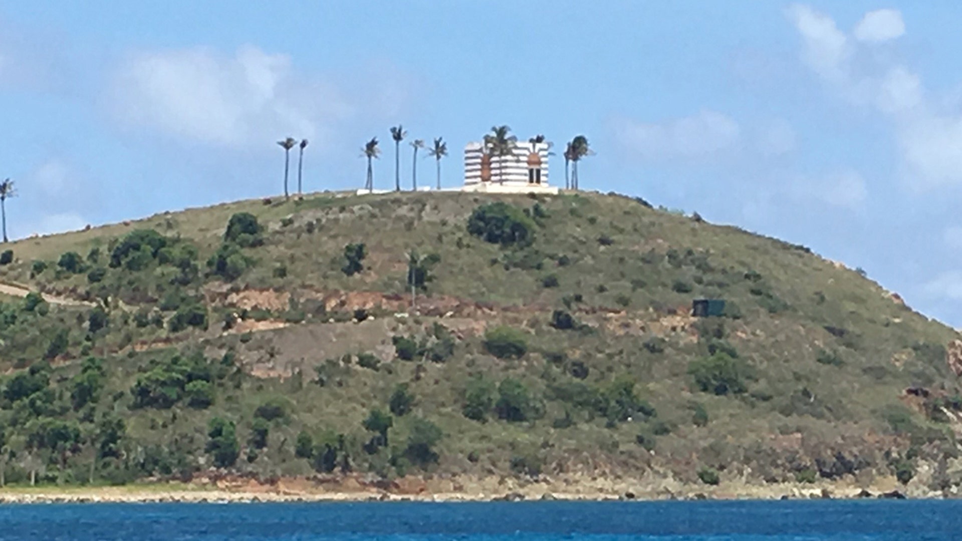 A view of a blue and white building on top of a hill and surrounded by palm trees on Jeffrey Epstein's Little St. James Island. 