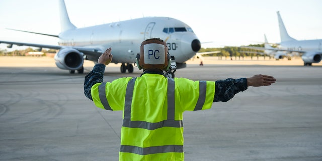 Aviation Machinist Mate 3rd Class Benjamin Harrell signals the crew of a P-8A Poseidon patrol aircraft. (U.S. Navy photo by Mass Communication Specialist 2nd Class Sean R. Morton/Released)