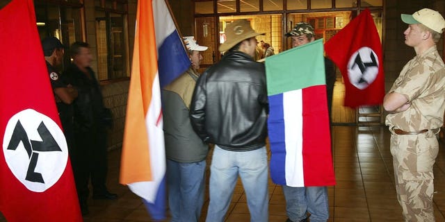 Supporters of the Afrikaner Resistance Movement (AWB) display an old South African flag, second from left, an old Afrikaner "Vierkleur" flag and swastika-like flags as they await the release of their leader, Eugene Terre'Blanche from prison in Potchefstroom, South Africa where he was granted parole after serving three years of an effective five year sentence for the 1996 attempted murder of a black security guard.