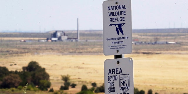 In this Wednesday, Aug. 14, 2019 photo, a sign designates a boundary of the Hanford Reach National Monument as the world's first large scale nuclear reactor, the B Reactor, is seen in the background where it sits unused on the Hanford Nuclear Reservation along the Columbia River near Richland, Wash. The Energy Department estimates it will cost between $323 billion and $677 billion more to finish the costliest cleanup, at the Hanford Site in Washington state where the government produced plutonium for bombs and missiles. (AP Photo/Elaine Thompson)