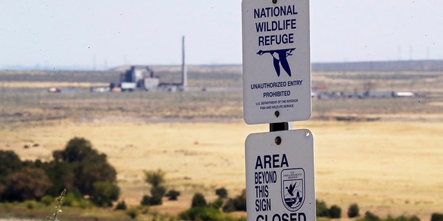 In this Wednesday, Aug. 14, 2019 photo, a sign designates a boundary of the Hanford Reach National Monument as the world's first large scale nuclear reactor, the B Reactor, is seen in the background where it sits unused on the Hanford Nuclear Reservation along the Columbia River near Richland, Wash. The Energy Department estimates it will cost between $323 billion and $677 billion more to finish the costliest cleanup, at the Hanford Site in Washington state where the government produced plutonium for bombs and missiles. (AP Photo/Elaine Thompson)