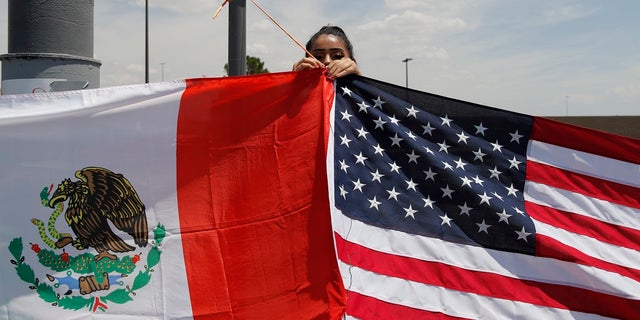 Maylin Reyes hangs a Mexican flag at a makeshift memorial near the scene of a mass shooting at a shopping complex Monday, Aug. 5, 2019, in El Paso, Texas. (AP Photo/John Locher)