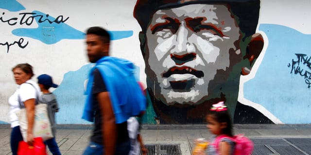 Pedestrians walk past a mural depicting the late President Hugo Chavez, in Caracas, Venezuela, Aug. 6, 2019. (AP Photo/Leonardo Fernandez)