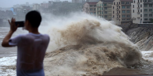 In this Aug. 9, 2019, photo released by Xinhua News Agency, a man uses his mobile phone to record waves crashing on the shore as typhoon Lekima approaches the Shitang Township of Wenling City in eastern China's Zhejiang Province. Typhoon Lekima stuck the coast south of Shanghai, knocking down houses and trees.
