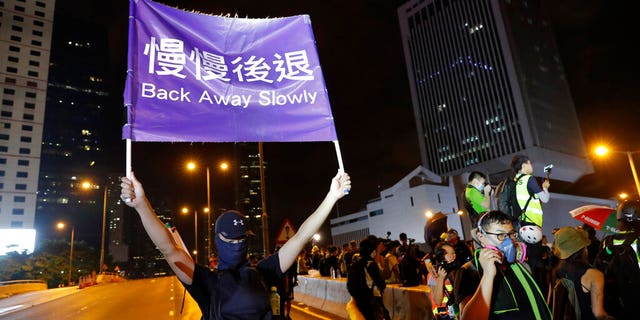 A demonstrator holding up a sign reading "Back away slowly" to encourage other demonstrators to leave, near the Chinese Liaison Office in Hong Kong on Sunday. (AP Photo/Vincent Thian)