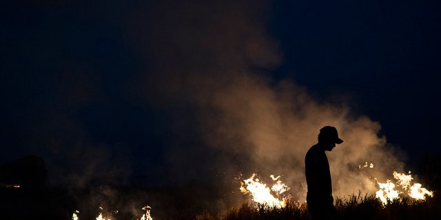 Neri dos Santos Silva, center, is silhouetted against an encroaching fire threat after he spent hours digging trenches to keep the flames from spreading to the farm he works on, in the Nova Santa Helena municipality, in the state of Mato Grosso, Brazil, Friday, Aug. 23, 2019. Under increasing international pressure to contain fires sweeping parts of the Amazon, Brazilian President Jair Bolsonaro on Friday authorized use of the military to battle the massive blazes. (AP Photo/Leo Correa)