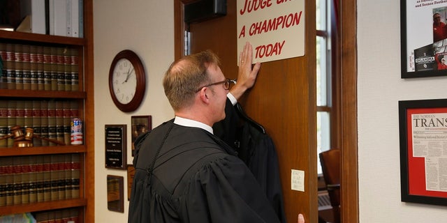 Judge Thad Balkman posing for a photo with the sign above his door before the court session to announce his decision in the oipiod lawsuit. (AP Photo/Sue Ogrocki, Pool)