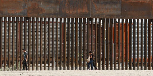 FILE - In this July 17, 2019, file photo, three migrants who had managed to evade the Mexican National Guard and cross the Rio Grande onto U.S. territory walk along a border wall set back from the geographical border, in El Paso, Texas. (AP Photo/Christian Chavez, File)