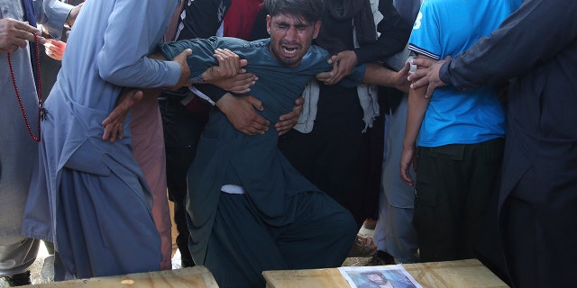 A relative wails near the coffins of victims of the Dubai City wedding hall bombing during a mass funeral in Kabul, Afghanistan. (AP Photo/Rafiq Maqbool)