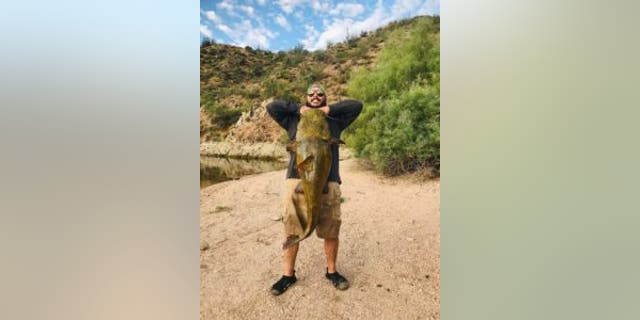 Erick Barrantes holding up a massive catfish that he has caught. 