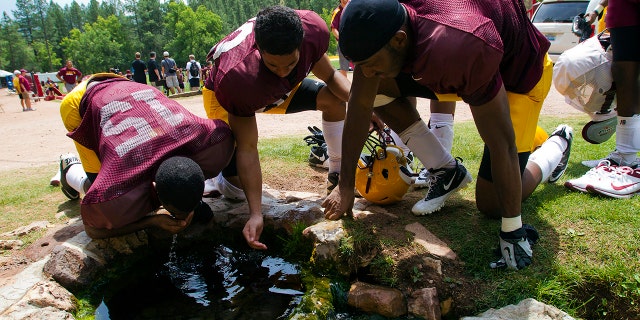 FILE - In this Aug. 15, 2012, file photo, Arizona State wide receivers Rashad Ross, left, JJ Holliday, center, and Alonzo Agwuenu drink water from a spring after NCAA college football practice at Camp Tontozona in Kohls Ranch, Ariz. (Michael Chow/The Arizona Republic via AP, File)
