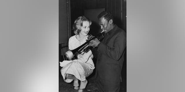 Jazz musician Miles Davis plays his horn as French actress Jeanne Moreau watches admiringly.