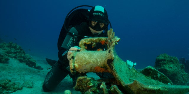 A diver inspects an amphora, or ancient jar, on the seabed.