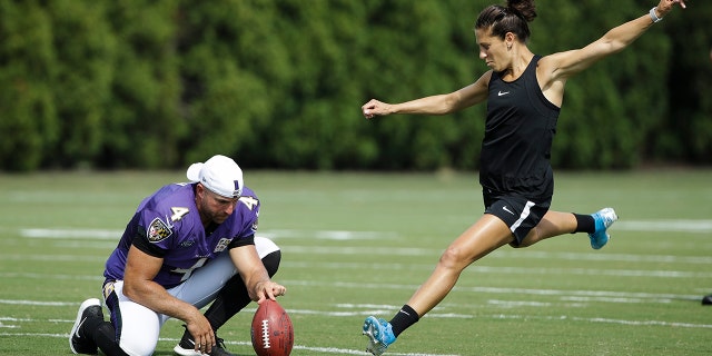 Baltimore Sam Koch of Ravens holds the ball for United States footballer Carly Lloyd tries to kick a field goal after Philadelphia Orly and Baltimore Ravens have a joint NFL football practice in Philadelphia, Aug. 20, 2019.