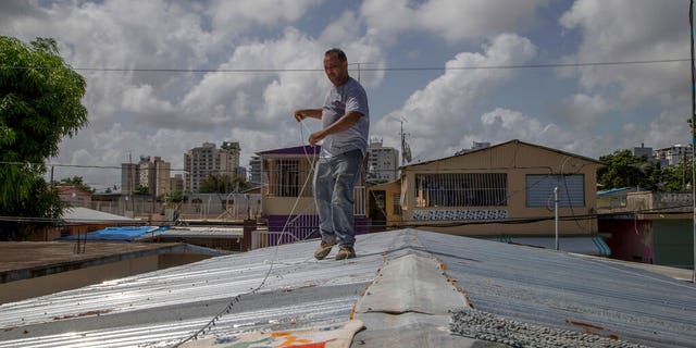 Jorge Ortiz works to tie down his roof as he prepares for the arrival of Dorian in San Juan, Puerto Rico, Tuesday, Aug. 27, 2019. (AP Photo/Gianfranco Gaglione)