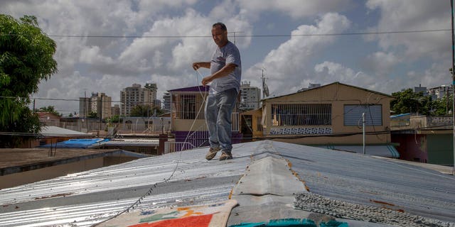 Jorge Ortiz works to tie down his roof as he prepares for the arrival of Dorian in San Juan, Puerto Rico, Tuesday, Aug. 27, 2019. (AP Photo/Gianfranco Gaglione)