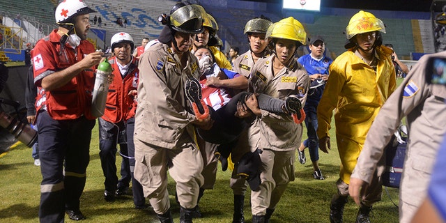 Firefighters carry a woman after three people died in riots before a soccer match when the fans attacked a bus carrying one of the teams, at the National Stadium in Tegucigalpa, Honduras.
