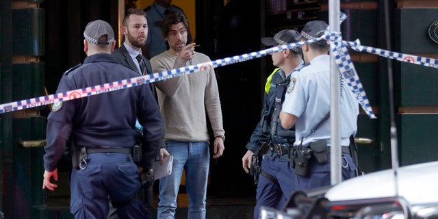 A man, center, points as he assists police at a building where a person has been found dead after a man attempted to stab multiple people in Sydney, Australia, Tuesday, Aug. 13, 2019.