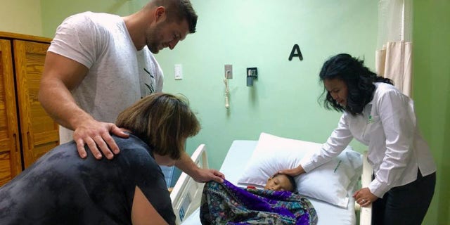 Tim Tebow praying with a patient at the Tebow CURE Hospital in the Philippines.