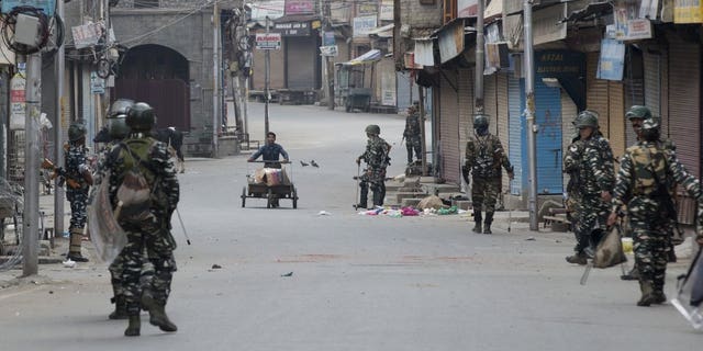In this Tuesday, Aug. 6, 2019 photo, a Kashmiri municipal worker pushes his cart filled with trash as Indian paramilitary soldiers patrol during curfew in Srinagar, Indian controlled Kashmir, Wednesday, Aug. 7, 2019. Authorities in Hindu-majority India clamped a complete shutdown on Kashmir as they scrapped the Muslim-majority state's special status, including exclusive hereditary rights and a separate constitution, and divided it into two territories.