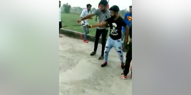 Dozens of men huddle around the treat after it is placed on the floor and begin to cheer on the man.