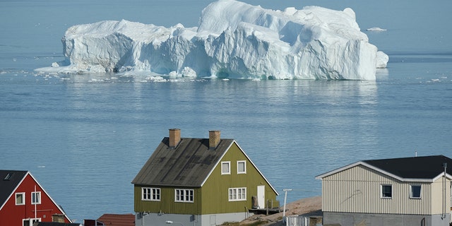 An iceberg floats in Disko Bay behind houses during unseasonably warm weather on July 30, 2019 in Ilulissat, Greenland. (Photo by Sean Gallup/Getty Images)