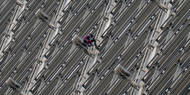 Alain Robert, a French rock and urban climber hangs on to Cheung kong centre building after hanging a large fabric displaying Chinese and Hong Kong flags, shaking hands and shining sun in Hong Kong, Friday, Aug. 16, 2019. (AP Photo/Vincent Thian)