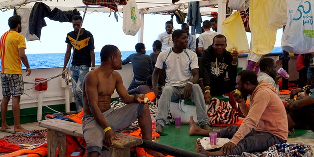 Migrants sit on the deck of the Open Arms vessel in front of island of Lampedusa as crew members described the situation on board as ''desperate,'' saying that a man threw himself in the water trying to reach land in plain view, while at the same moment a woman suffered a panic attack. (AP Photo/Francisco Gentico)